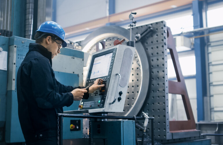 CNC-operator met veiligheidshelm bedient het paneel van een machine